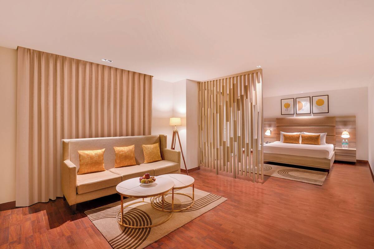 A modern hotel room with a sofa, a round coffee table, a bed, and a nightstand.