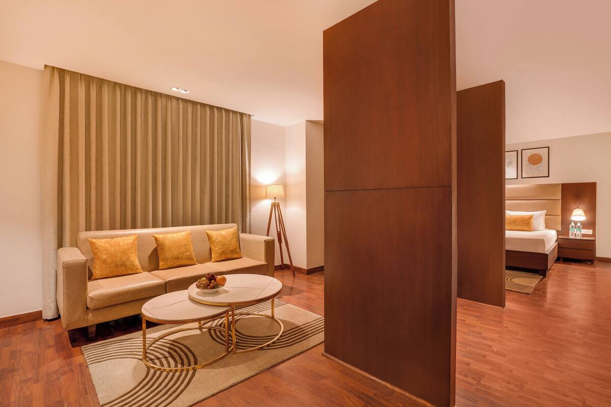 A hotel room with a sofa, a round coffee table, a lamp, and a bed.