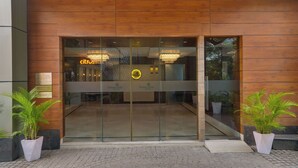 Een hotelentree met glazen deuren, een neonreclame en potplanten.