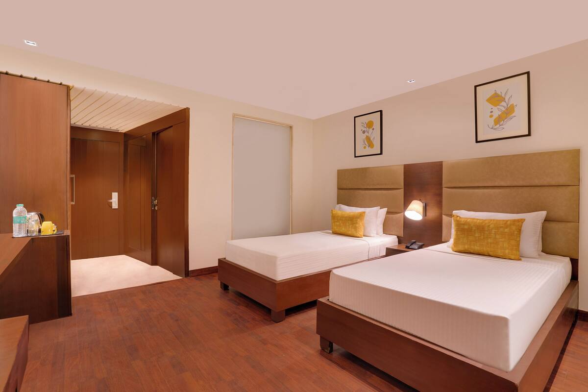 A hotel room with two beds, wooden flooring, a wardrobe, and a small table with toiletries.