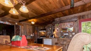 A rustic wooden interior with a wooden dining table, hanging lights, and a wicker chair. - Farmhouse located on river with Mountain View-Wifi/Cable (Walland)