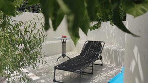 Un espace extérieur ensoleillé avec une piscine, deux chaises longues, une petite table et une plante en pot.