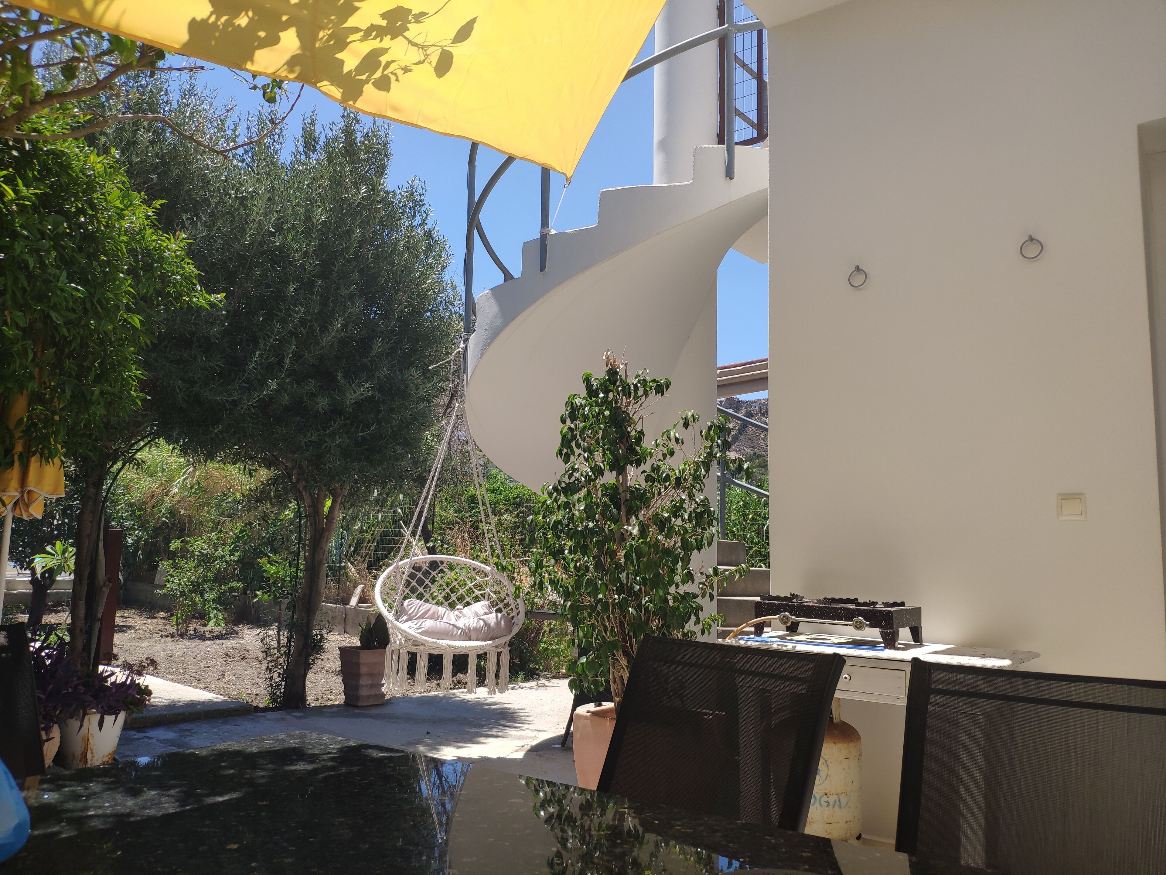 A modern outdoor seating area with a white chair, a hanging chair, and a dining table.