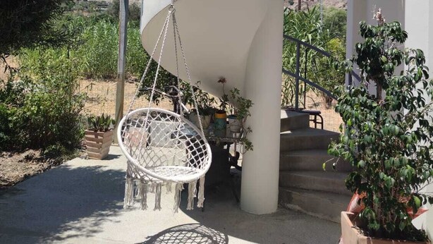 Un escalier en colimaçon menant à un balcon agrémenté d’une chaise suspendue et de plantes en pot.
