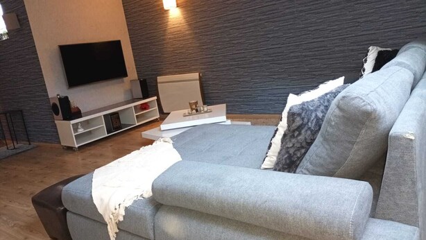 Una sala de estar moderna con un sofá gris, un televisor de pantalla plana montado en la pared y un mueble blanco para entretenimiento.