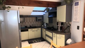 Cocina compacta con refrigerador, estufa y armarios. Cuenta con tragaluz sobre el fregadero y un pequeño comedor con mesa y sillas.