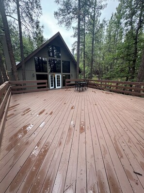 Une terrasse en bois avec un bâtiment en arrière-plan, le tout entouré d’arbres.