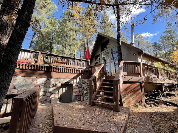 A cabin with a stone foundation, wooden deck, and a staircase leading to a balcony.