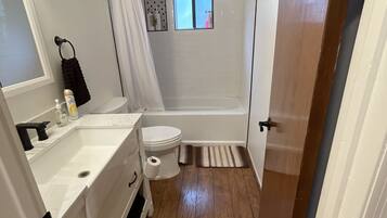 Un baño pequeño con lavamanos, inodoro y zona de ducha blancos.