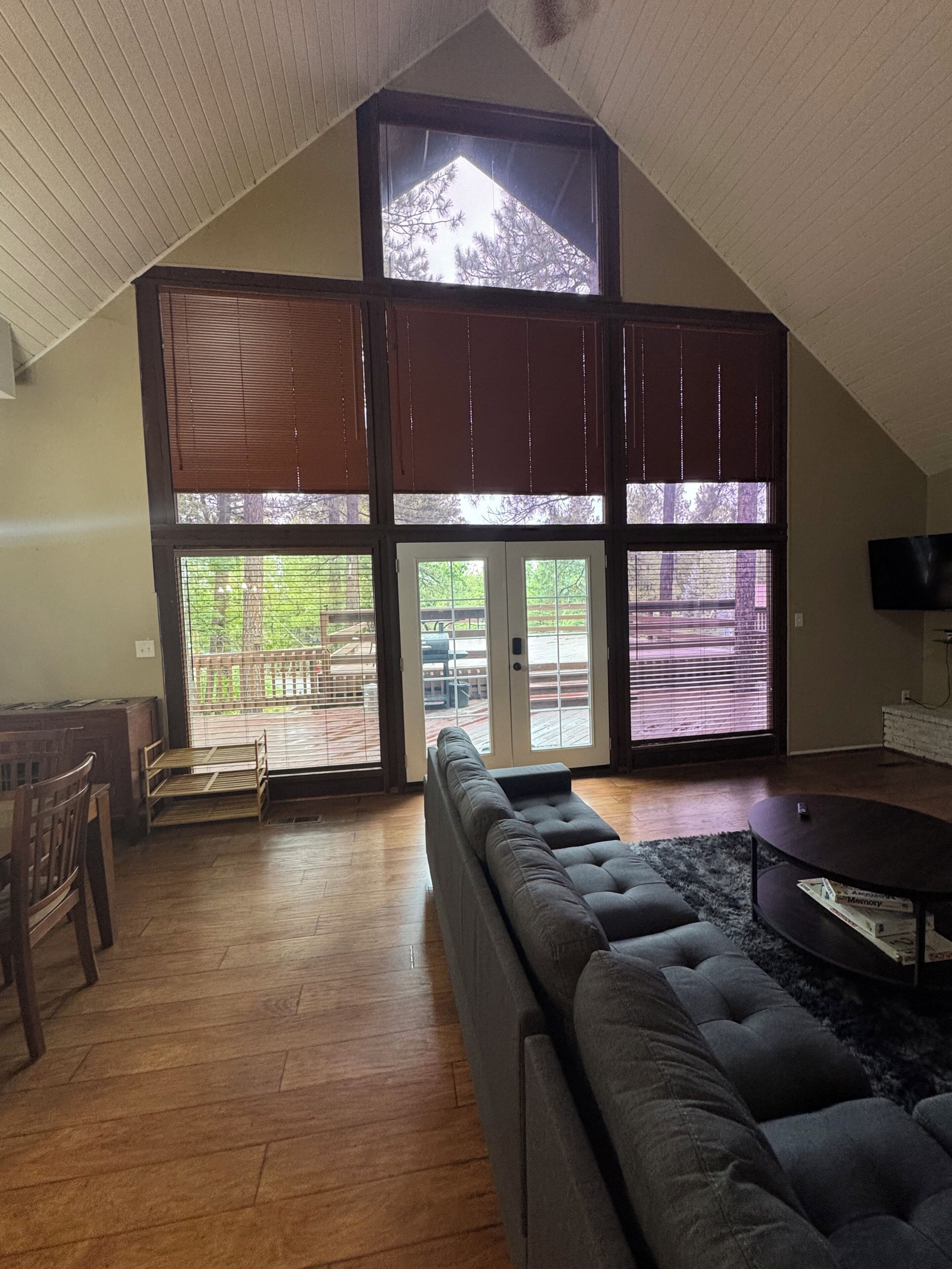 Een ruime woonkamer met een hoge plafond, grote ramen, een hoekbank en een flatscreen-tv.