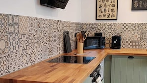Eine Küche mit einer Holzausziehtheke, einem eingebauten Backofen und einem grünen Schrank. An der Wand befinden sich zwei gerahmte Pflanzenbilder.