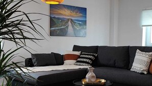 Ein modernes Wohnzimmer mit einem dunkelgrauen Sofa, einem runden Couchtisch, einer Zimmerpflanze und einem Gemälde an der Wand.