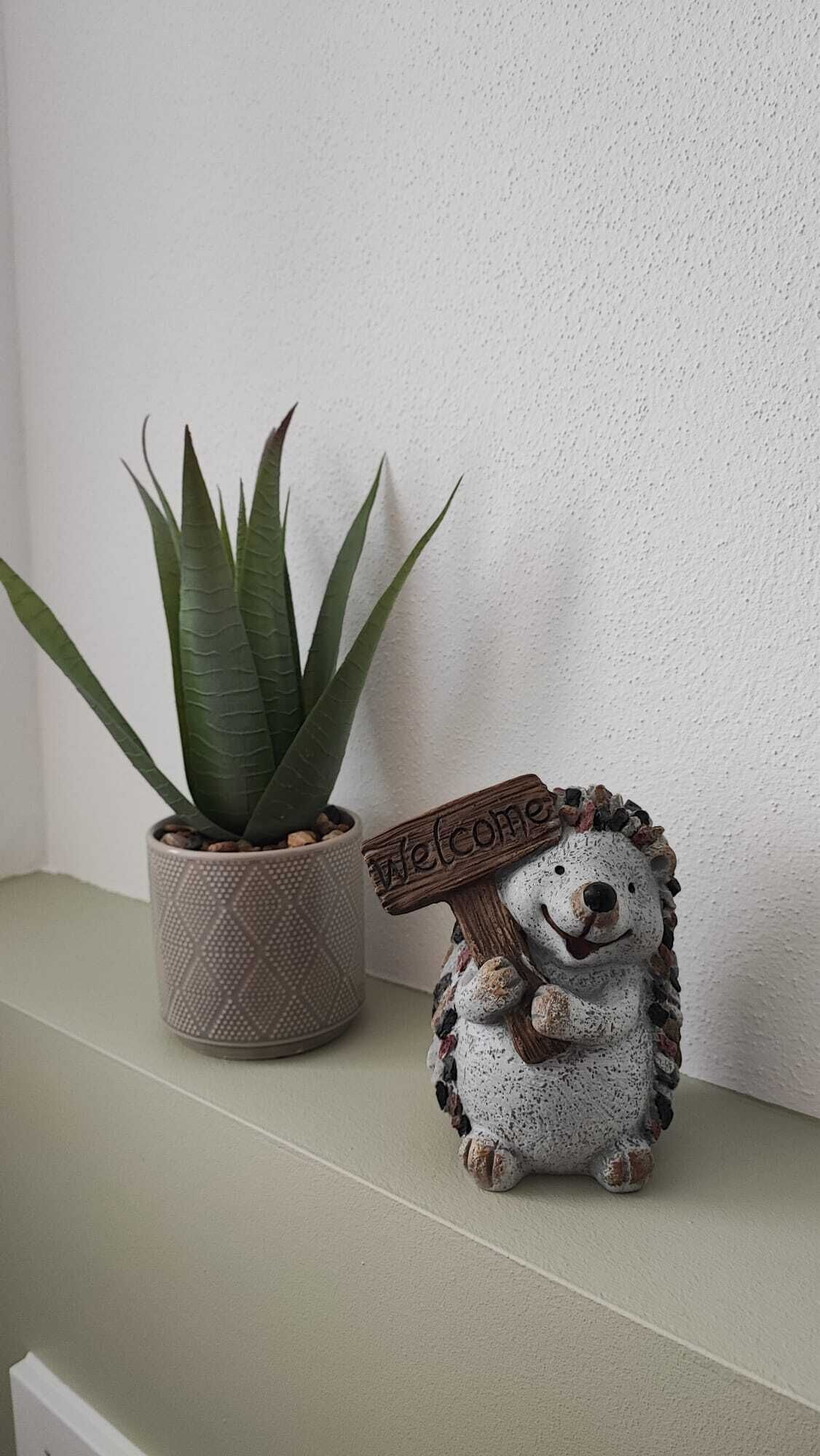 Una planta pequeña en maceta y una figura de erizo de cerámica sobre una estantería.