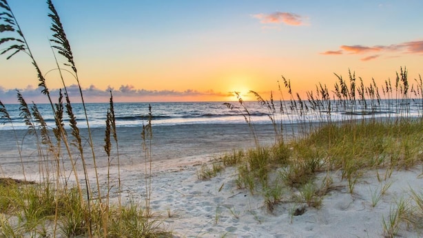 A beach with sand and grass in the foreground, and the ocean in the background. - Beautiful beach cottage 1/2 mile to the Sandy Shore! (Fernandina Beach)