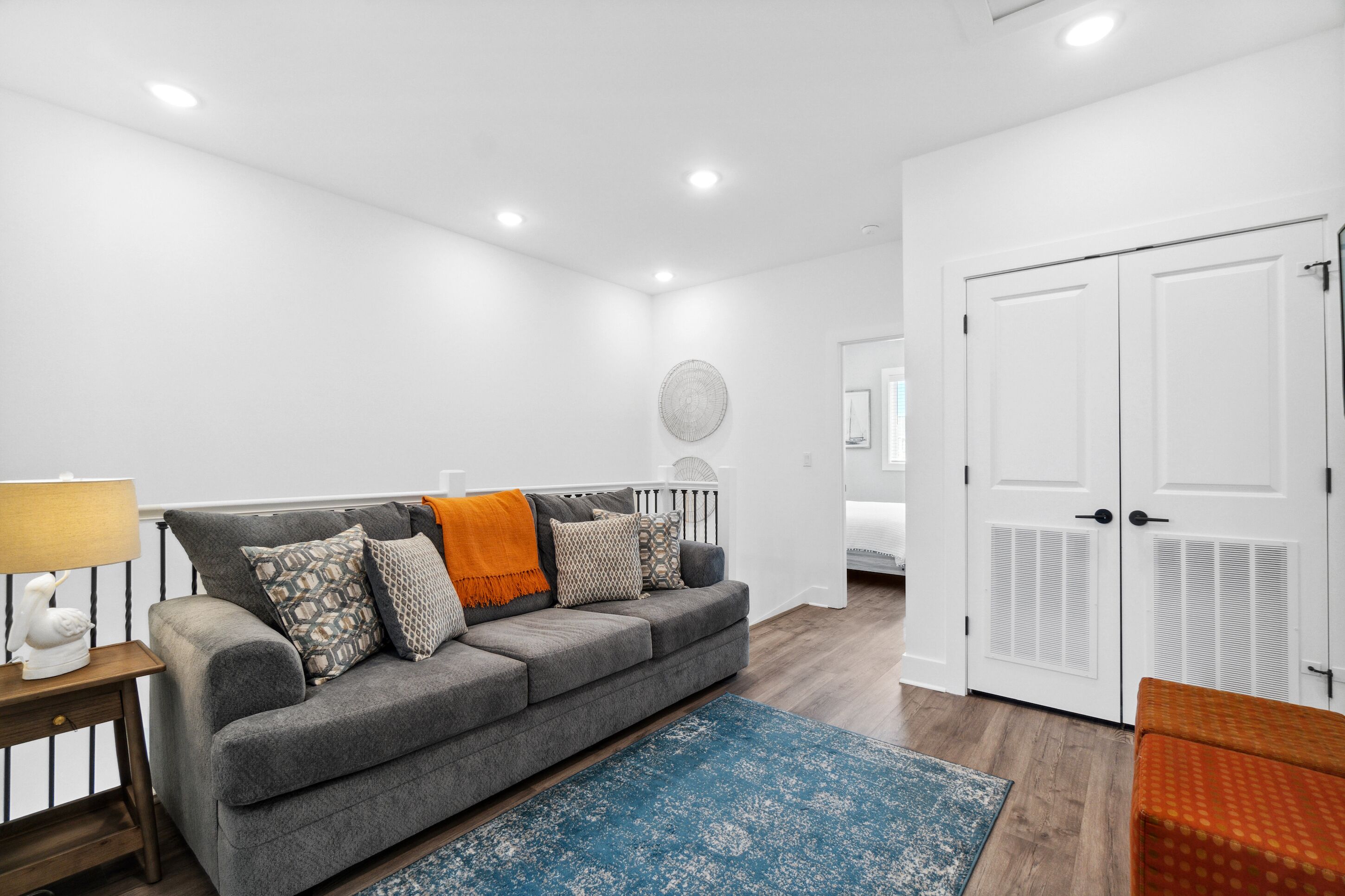 A modern living room with a grey sofa, patterned cushions, a blue rug, and white doors.