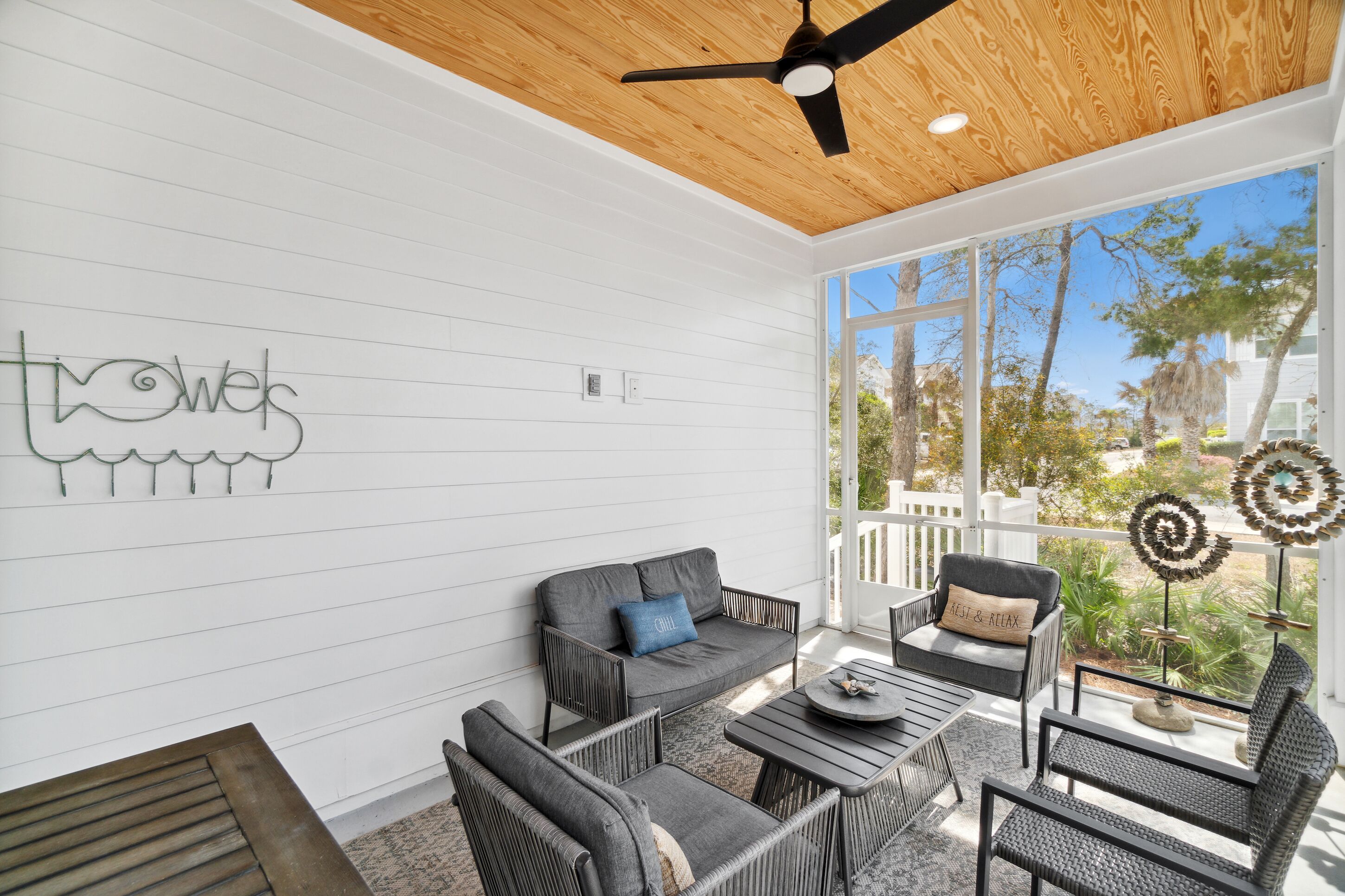 A sunlit patio with a wooden ceiling, white walls, and a large window offering a view of the outdoors.