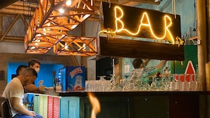 A bar area with a neon sign, glasses, and a bottle of Postobon beer. - Hotel Campestre La Aldea (Montenegro)