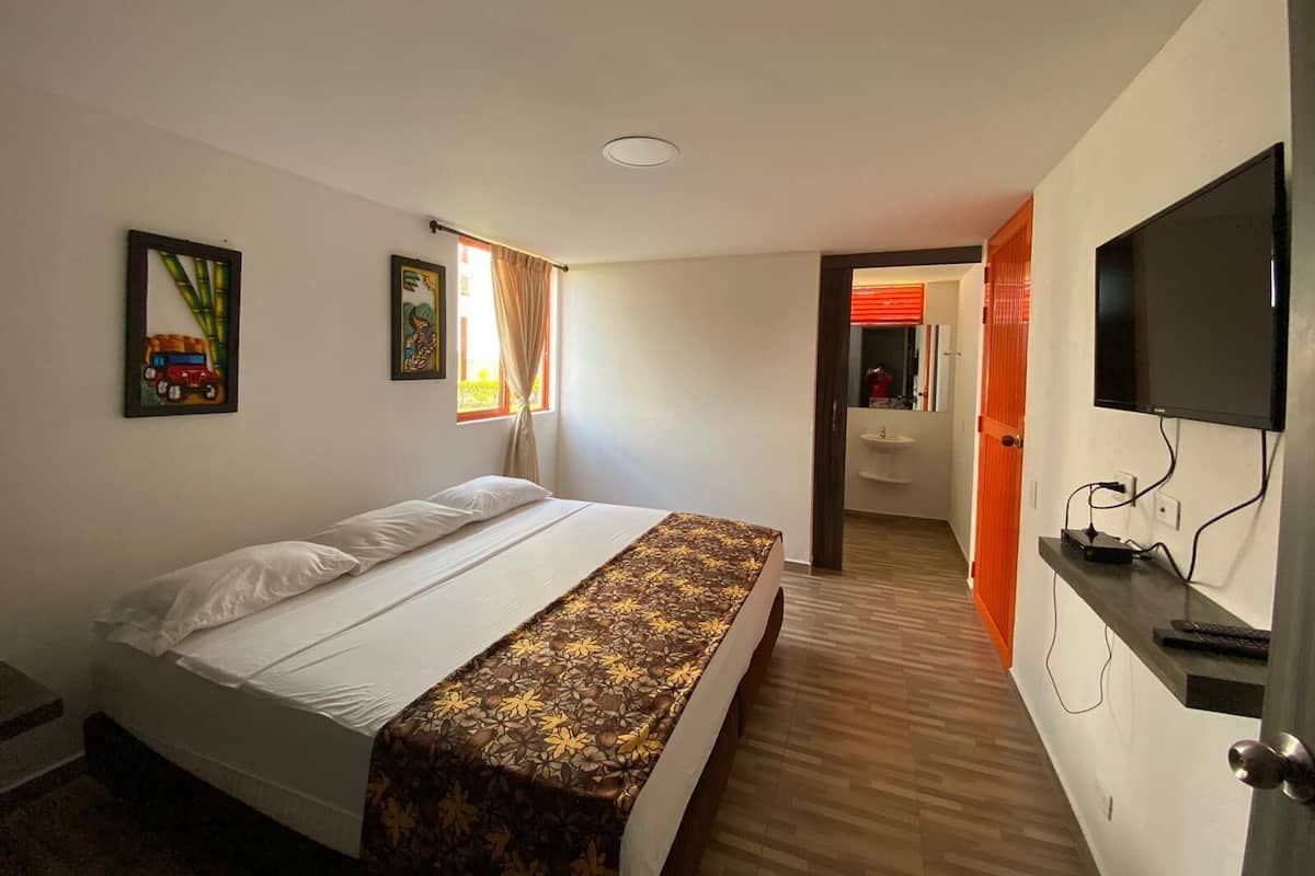 A hotel room with a bed, a TV, a bathroom with a sink, and a window with curtains.