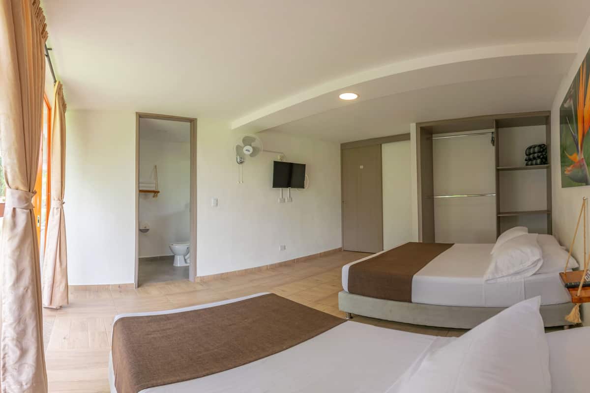 A hotel room with two beds, a TV, a painting, and a bathroom visible through an open door.