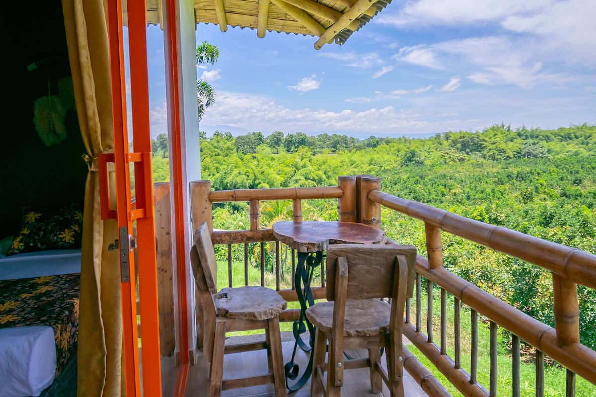 A balcony with a table and chairs, a wooden railing, and a view of a lush green landscape.
