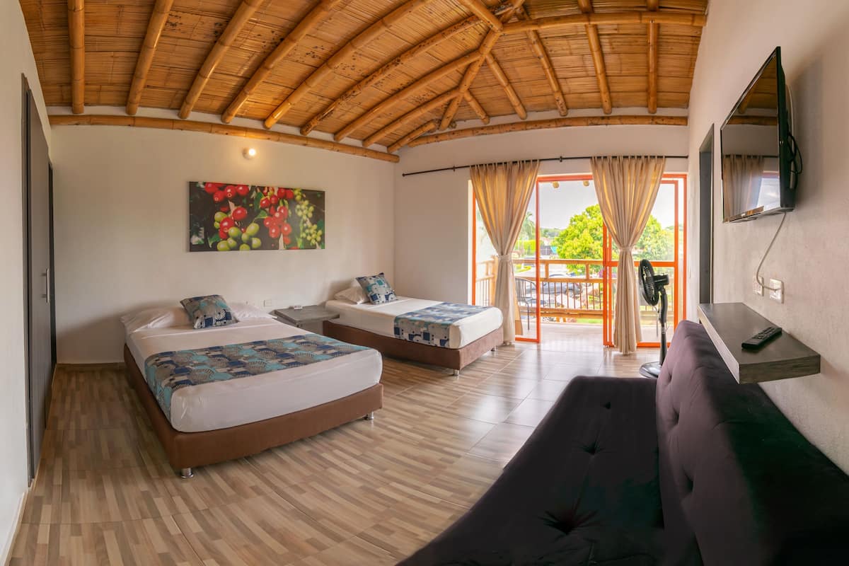 A room with two beds, a sofa, a TV, and a balcony with curtains.