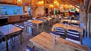 A restaurant with wooden tables and chairs, hanging woven light fixtures, and a kitchen area in the background. - Hotel Campestre La Aldea (Montenegro)
