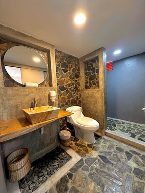 A bathroom with a stone wall, a wooden vanity, a white toilet, and a mirror. - Hotel Campestre La Aldea (Montenegro)