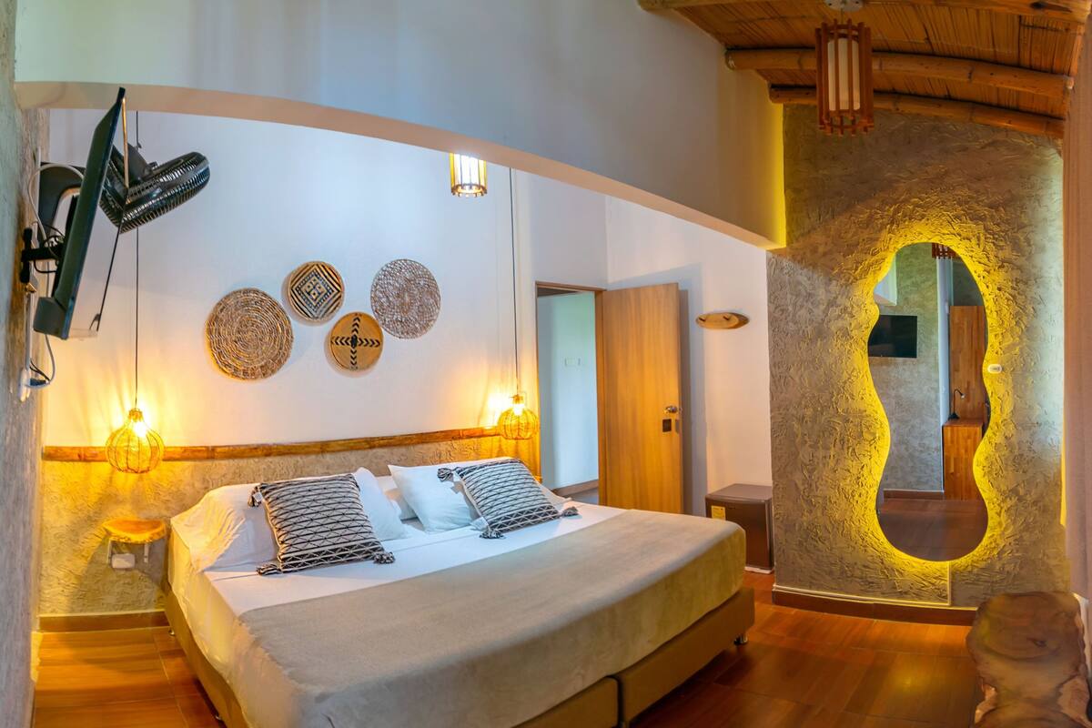 A bedroom with a large bed, two bedside tables, a wall-mounted fan, and a unique textured wall feature.