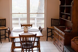 A dining area with a wooden table and chairs, a buffet cabinet, and a large window with a view of trees.