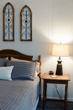 A neatly made bed with a quilted cover, a bedside table with a lamp, and two decorative wall mirrors.
