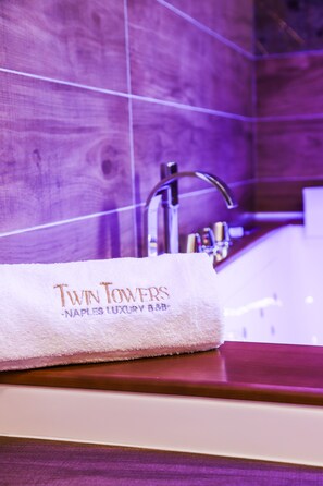 A bathroom with a white towel on a wooden counter, a sink, and a mirror. - Twin Towers Naples Luxury  (Naples)