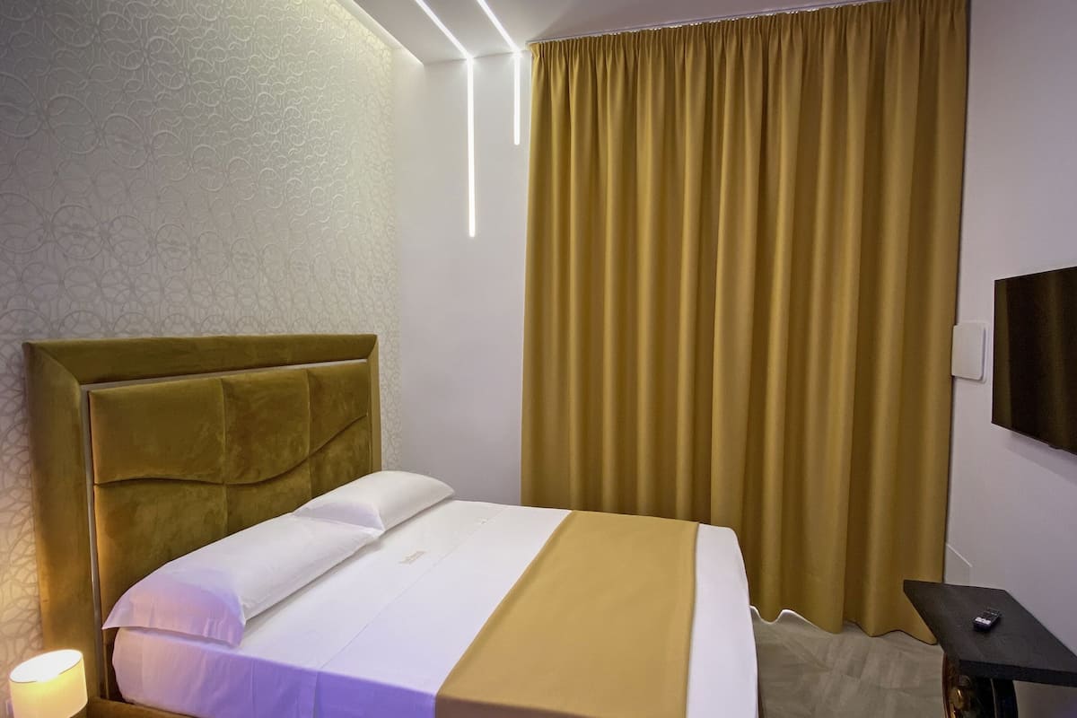 A hotel room with a bed, a nightstand, a lamp, a TV, and a curtain.