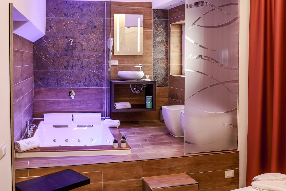 A modern bathroom with a bathtub, shower, and toilet. There is a vanity with a mirror and a sink. A small table and a towel are on the floor.
