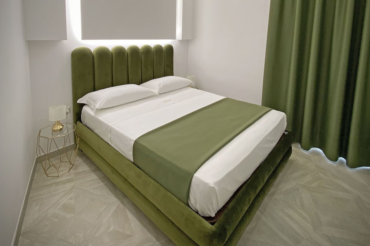 A modern bedroom with a green bed, white bedding, and a geometric-patterned floor.