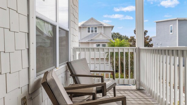 A covered porch with a wooden chair and a white railing. - 30A Beach House - Whatcha Dune by PHG (Panama City Beach)