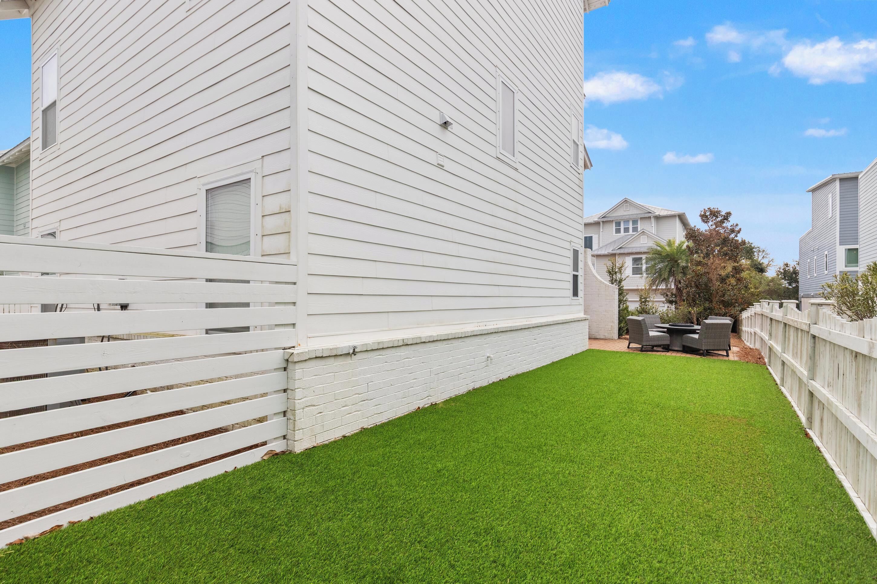 A white building with a fenced backyard and a patio area with outdoor furniture.