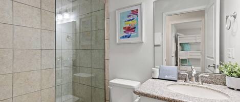 A modern bathroom with a glass shower enclosure, a white toilet, a granite countertop sink, and a framed artwork on the wall.