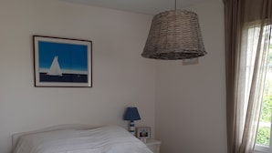 Una camera da letto con un letto grande, una lampada in vimini sospesa, un quadro incorniciato al muro e una finestra con tende.