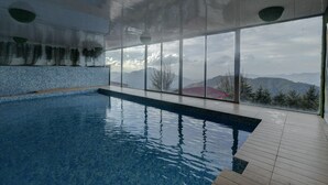 An indoor swimming pool with a view of mountains through large windows. - Tarika Resort and Spa (Kandaghat)
