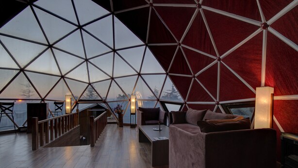 A spacious interior with a geometric ceiling design, wooden flooring, and a seating area with a sofa and a table. - Tarika Resort and Spa (Kandaghat)