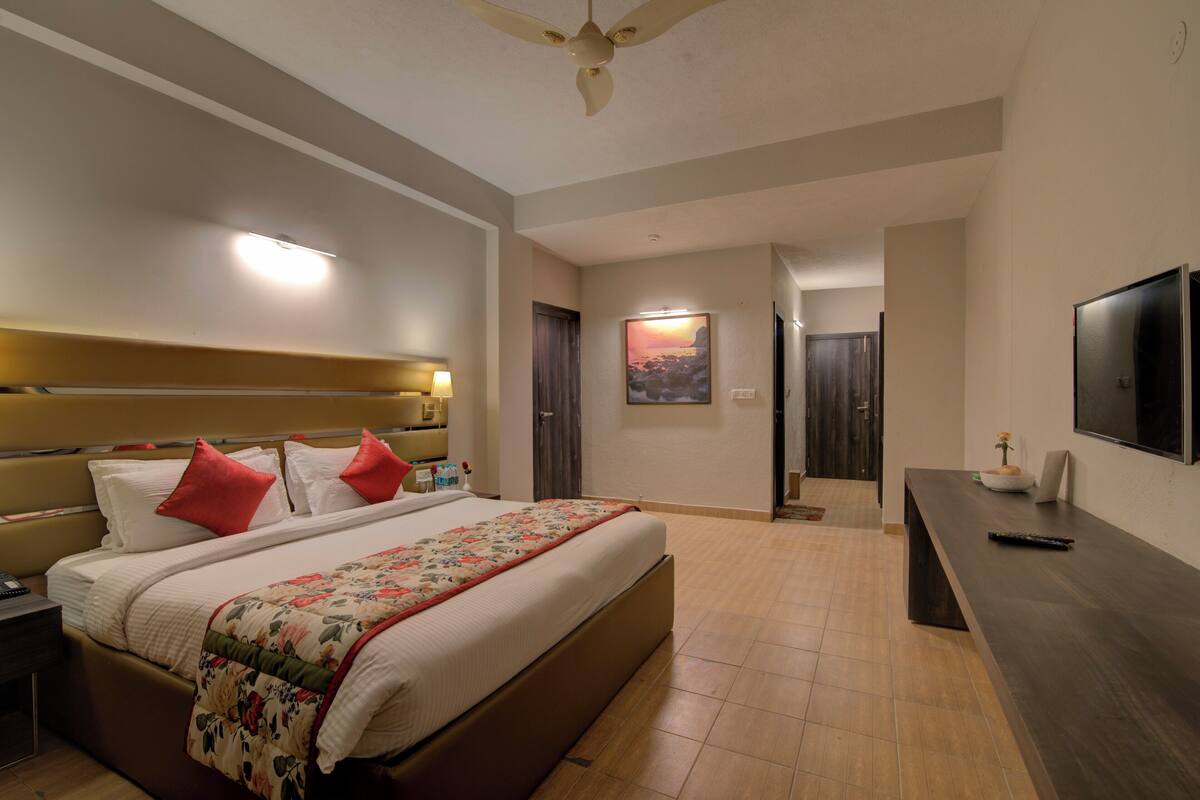 A hotel room with a large bed, bedside tables, a desk with a chair, a flat-screen TV, and a ceiling fan.