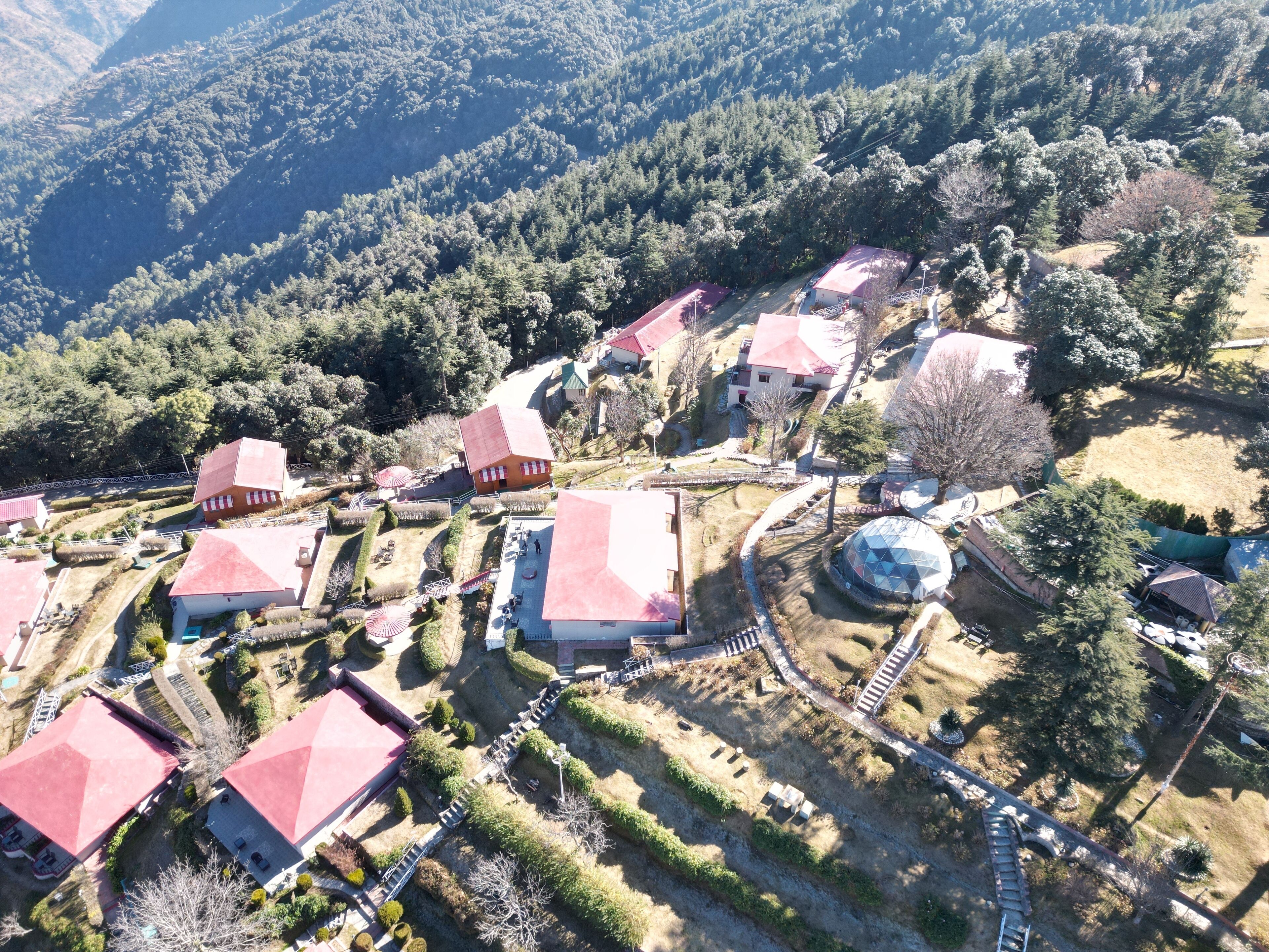 Vista aérea de un pueblo con casas de tejados rojos, un edificio de forma abovedada y un camino sinuoso.