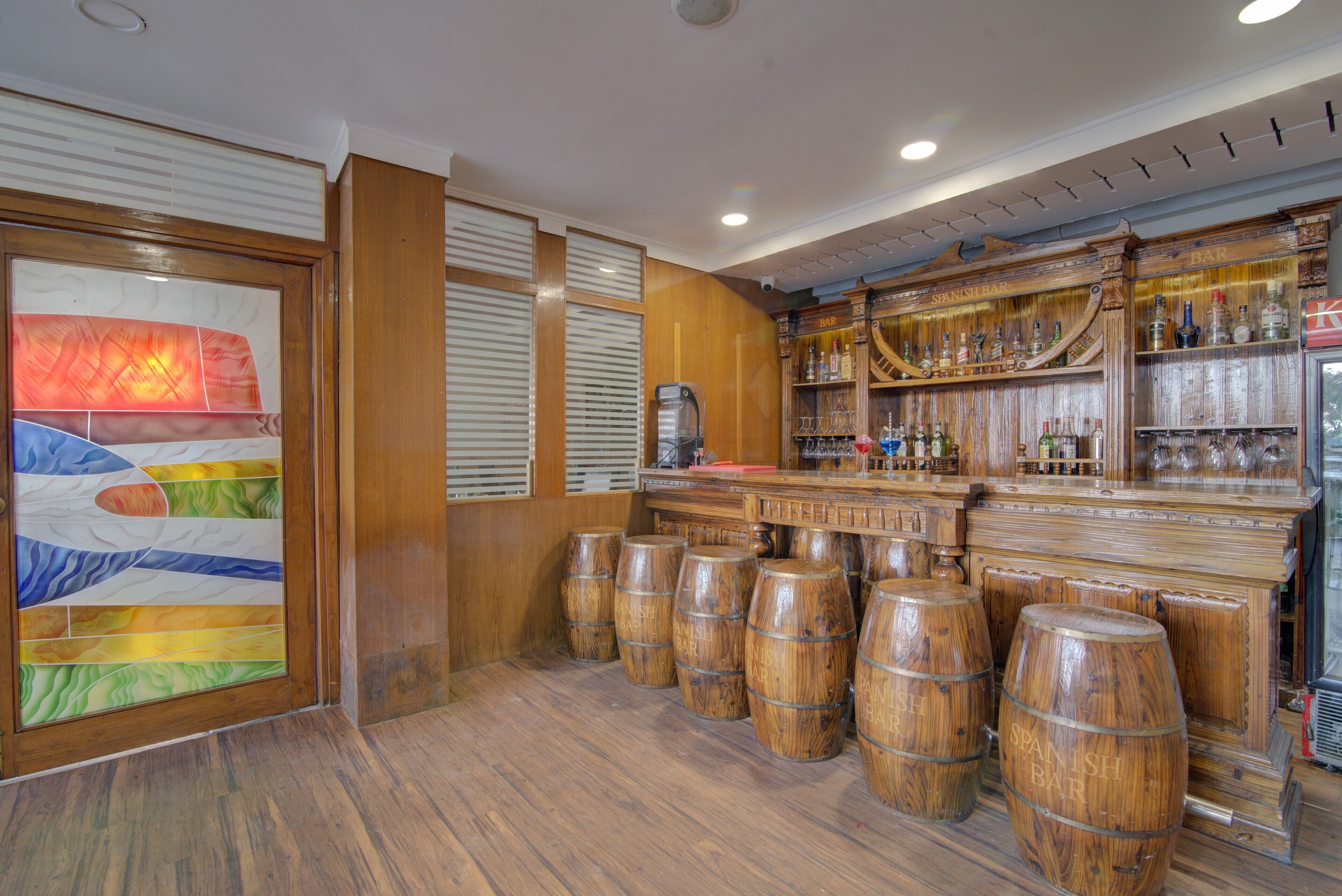 A bar area with wooden barrels, a bar counter, and a large stained glass window.