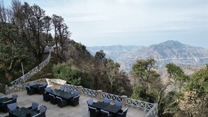 An outdoor patio with multiple tables and chairs, surrounded by stone walls and a white railing. - Tarika Resort and Spa (Kandaghat)
