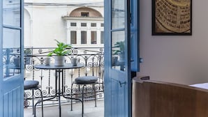 Un balcón con mesa y sillas, una planta en maceta y vistas de un edificio con ventanas de arco.