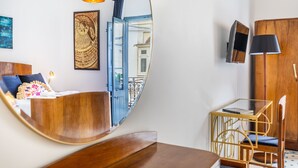 Una habitación moderna con una cama de madera, un espejo curvo, una mesa de vidrio con una silla y un televisor montado en la pared.