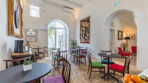 Un hall de hotel con varias mesas y sillas para comer, un tapiz grande y vistas al exterior.