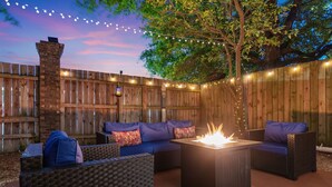 Un patio al aire libre con mobiliario de mimbre, un brasero y luces colgantes.