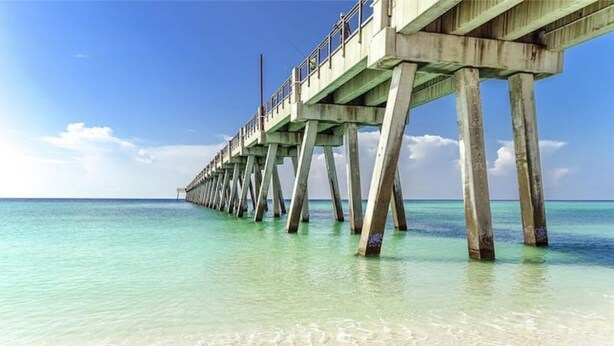 Un muelle que se adentra en aguas turquesas cristalinas, con una playa arenosa al final.