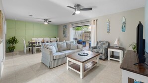 Una sala de estar con sofá, mesa de centro y televisor. Hay un comedor con sillas y mesa.